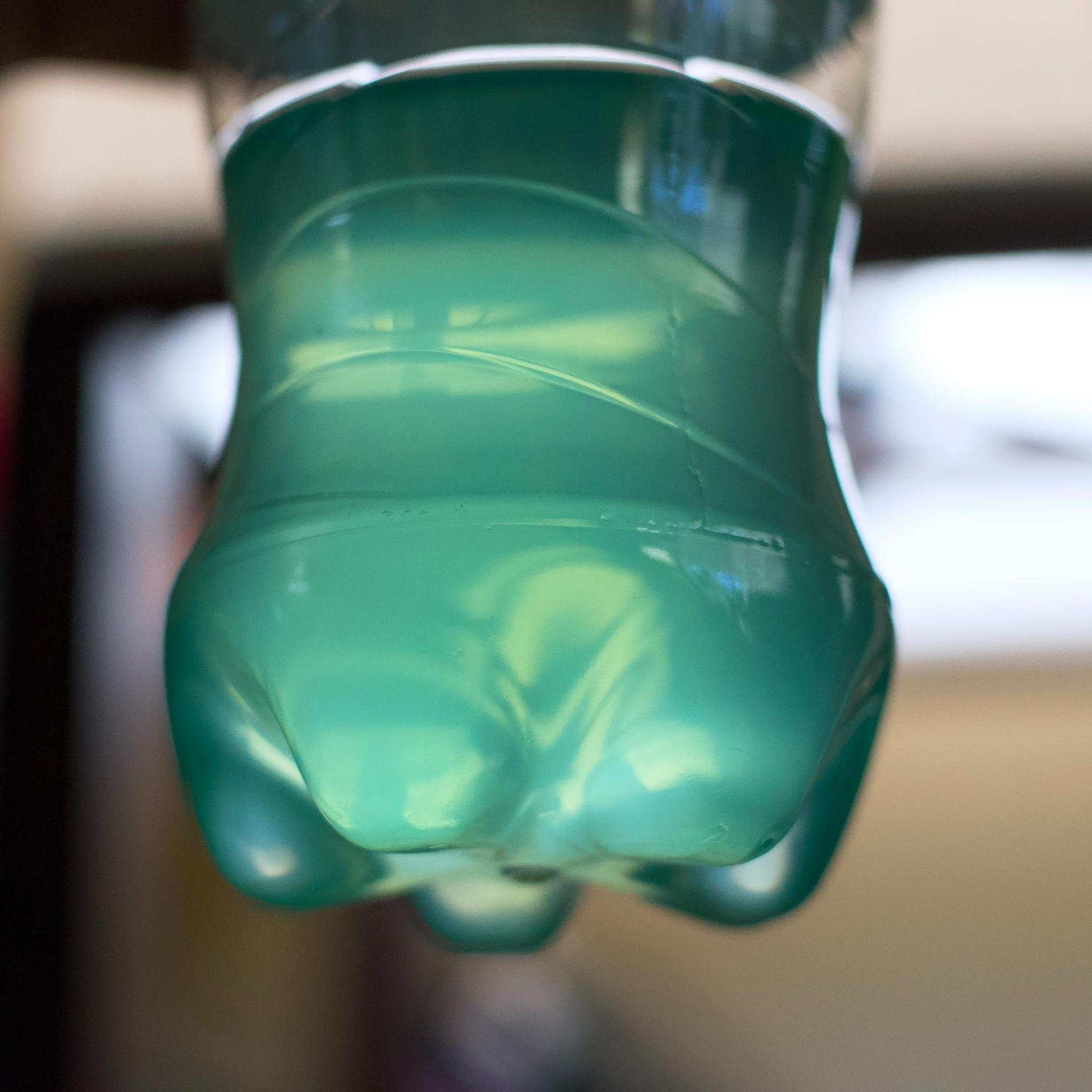 A partially fillled plastic bottle of Baja Blast with the background gently out of focus. The soda is glowing with a blue green light from the sun